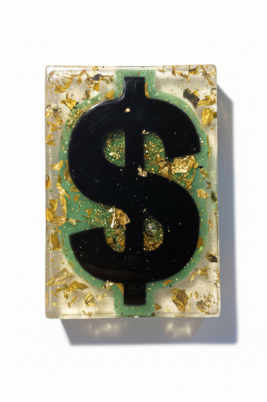 A square resin tile featuring a black infinity symbol over a green background, embedded with gold foil flakes on a light gray surface.