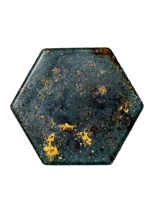 A hexagonal dark teal-green stone or resin piece with gold leaf inclusions, photographed on a plain off-white surface.